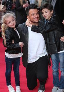 Peter Andre kneeling with his two children on a red carpet.
