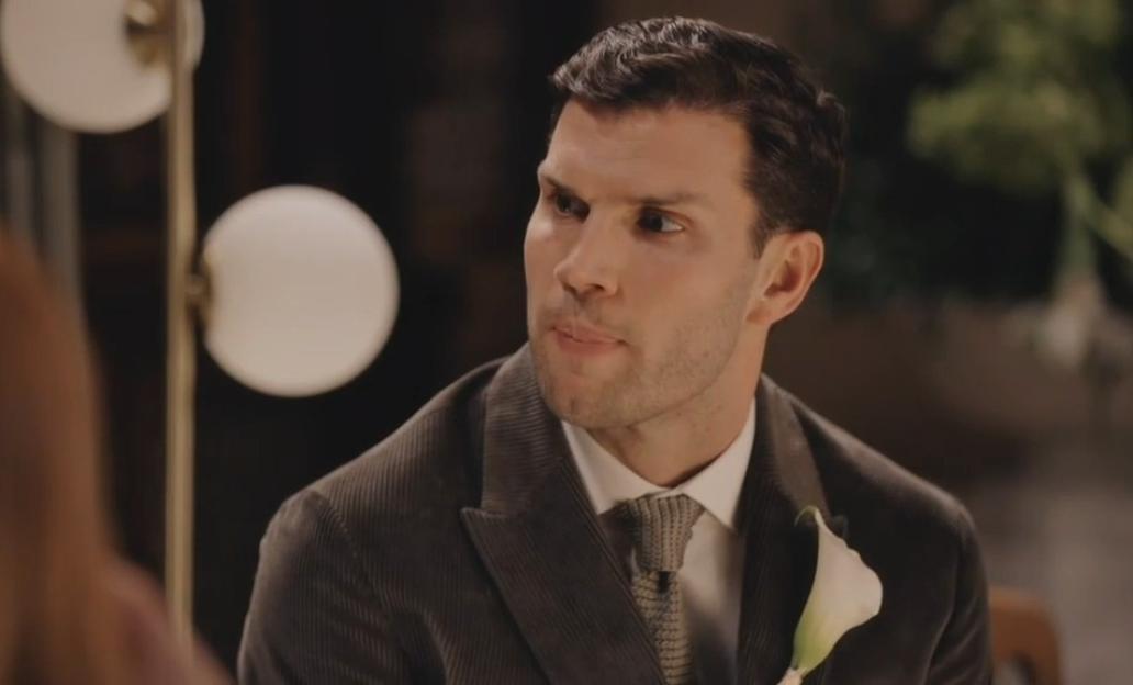 Reiss looks to his right, wearing a corduroy suit and a white calla lily boutonnière.