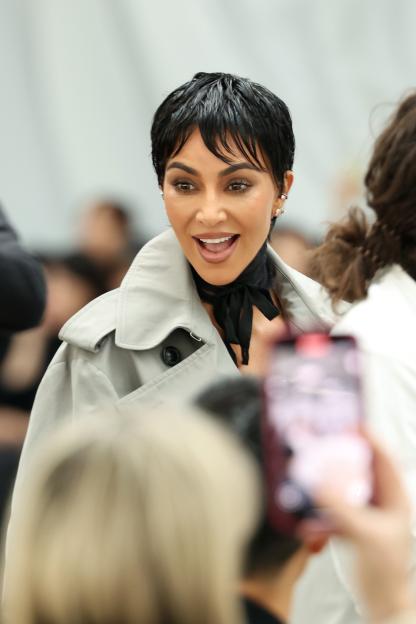 Kim Kardashian in a light gray trench coat and black scarf with a short, dark hairstyle, at Paris Fashion Week.