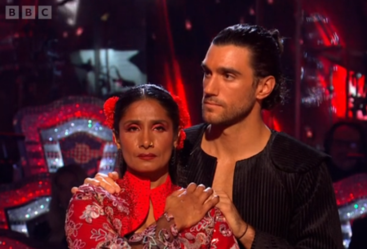 A male and female dancer, both with sad expressions, stand side by side on a stage.