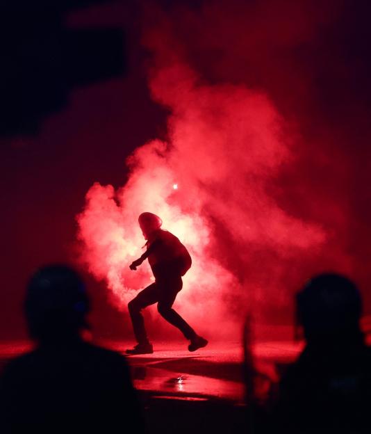 A pro-Palestine demonstrator with a flare in red smoke during a protest.
