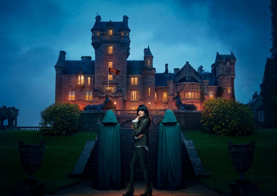 Claudia Winkleman on the steps of a castle with two cloaked figures.