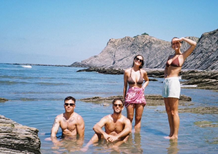 Four friends at the beach. Two men are in the water, and two women are standing in shallow water.