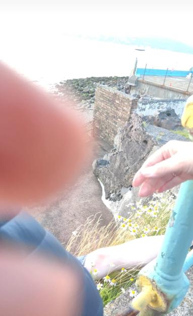 A man dangling from a collapsed sea railing.
