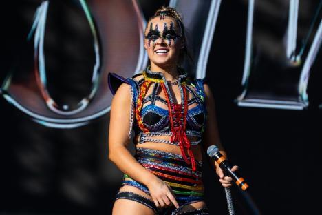 A performer in a colorful, sequined costume holds a microphone at Mighty Hoopla 2024.