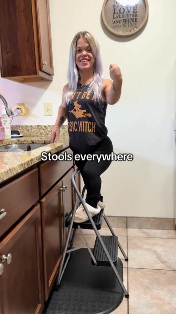 A woman with dwarfism standing on a step stool in a kitchen.