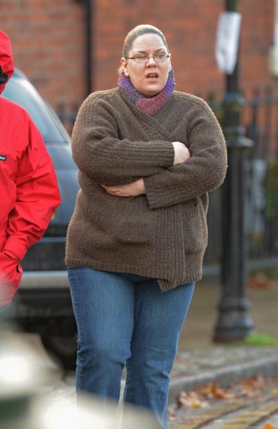 A woman wearing glasses and a brown sweater has her arms crossed