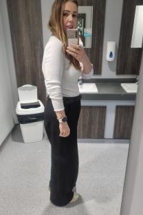 Woman in white top and black pants taking a selfie in a bathroom.