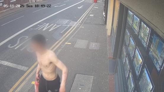 Surveillance image of a shirtless man carrying a fire extinguisher.