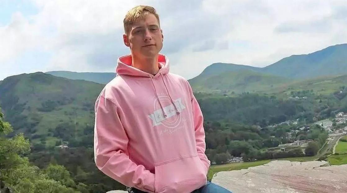 Man in pink hoodie in mountainous landscape.