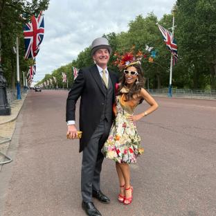 Panthea Parker and a man in formal wear stand on a street lined with British flags.