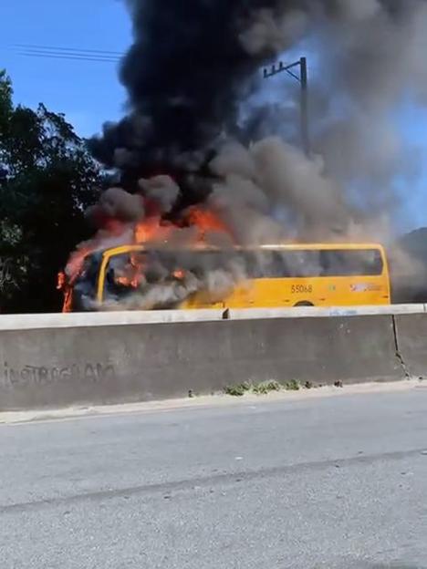A yellow bus engulfed in flames with thick black smoke rising into the sky.