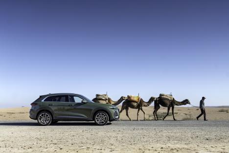 A green SUV parked on a desert road next to a camel caravan.