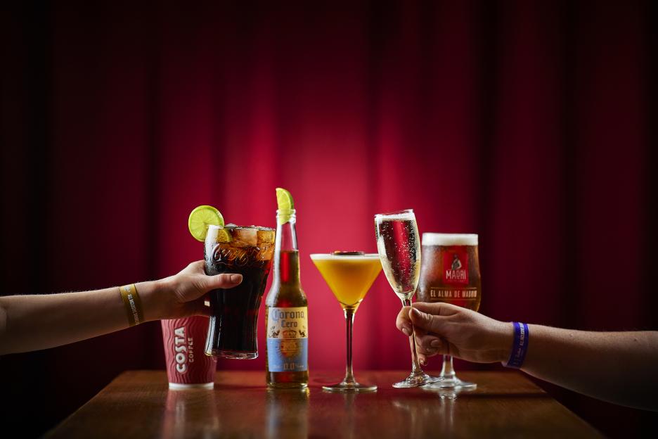 Two people toasting with drinks including Coca-Cola, Corona Zero, a cocktail, champagne, and beer.