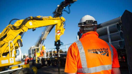 Network Rail worker in safety gear, with railway equipment in the background.