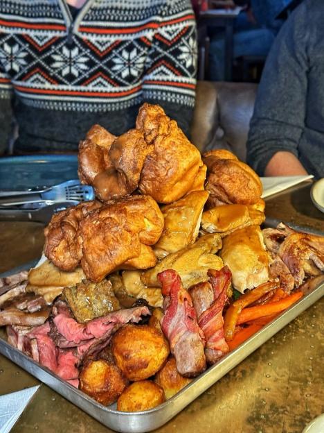 A platter of roast dinner with Yorkshire puddings, meat, roasted vegetables, and stuffing.