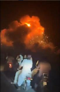 People on motorcycles watching a large fire at night.