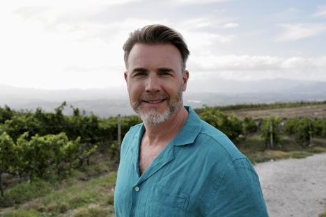 Gary Barlow in a teal shirt, smiling in a vineyard.