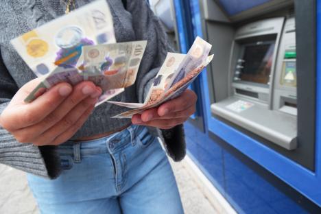 Woman counting British banknotes after withdrawing cash from an ATM.