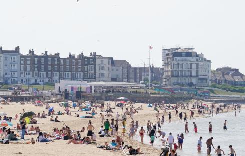 Crowded beach with people sunbathing and swimming.