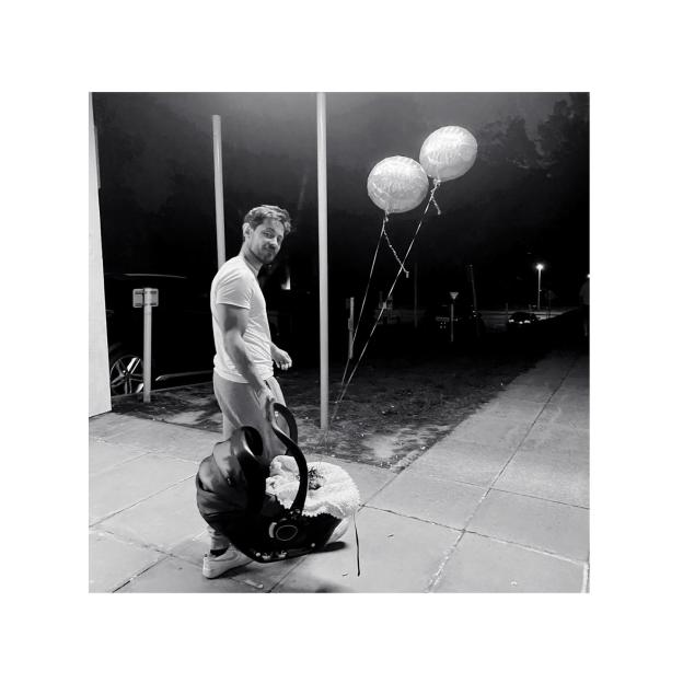 Elliot James Langridge carrying a baby in a car seat with two "Baby Boy" balloons floating nearby.