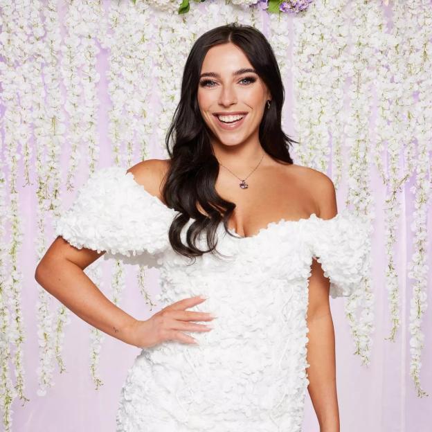 Erica Roberts smiling in a white off-the-shoulder dress with a textured floral pattern.