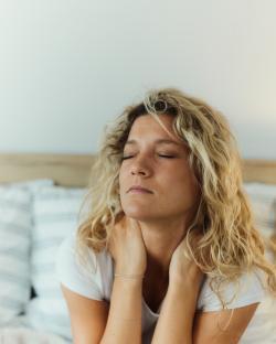 Woman in bed holding her neck in pain.