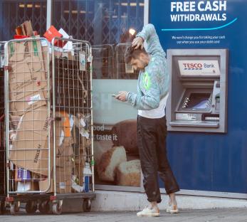 Man using phone at ATM, recycling bin nearby.