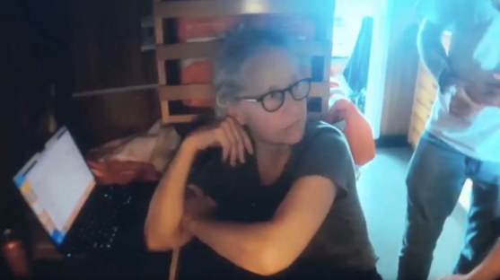 Screenshot of a woman sitting at a laptop.