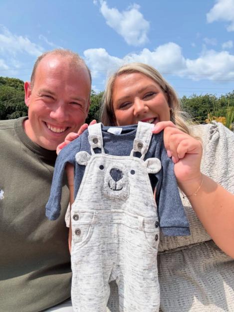 Couple holding baby clothes; gender reveal.