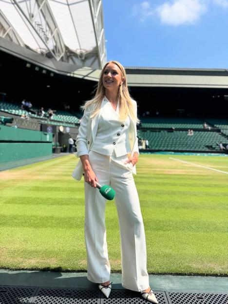 Woman in white suit holding microphone at Wimbledon.