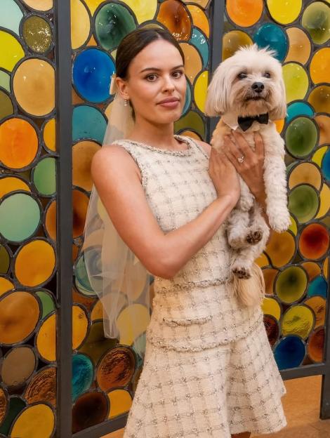 Woman in a wedding dress holding a small white dog in a bowtie.