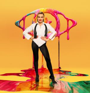 Ella Rae Wise in front of a colorful paint splatter design.