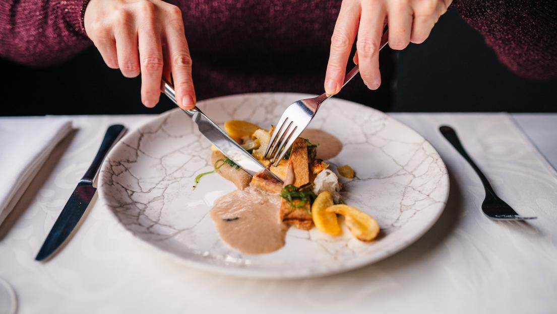 Person cutting into a plate of smoked tofu with potatoes, pumpkin sauce, onion, and seaweed.