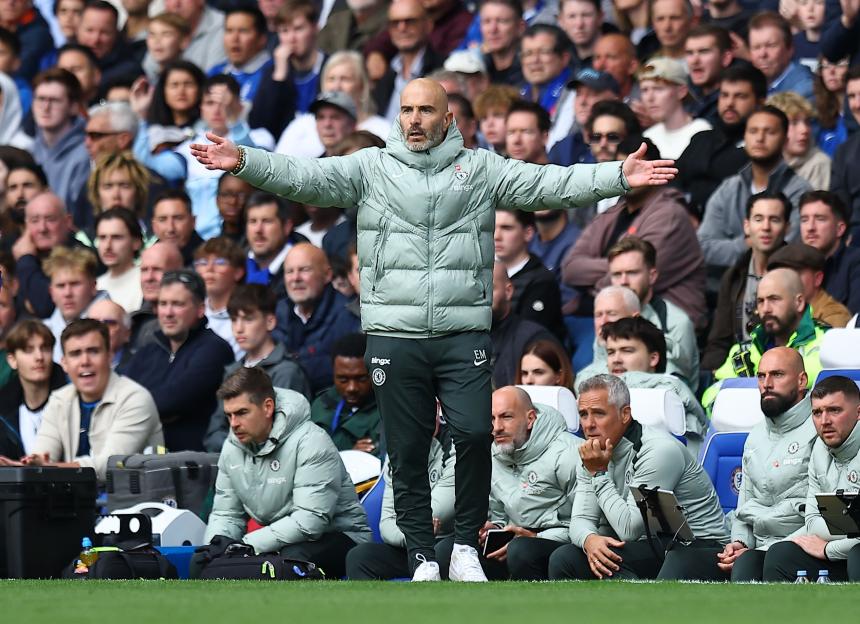 Enzo Maresca, Chelsea manager, reacting during a match with arms outstretched and a crowd in the background.