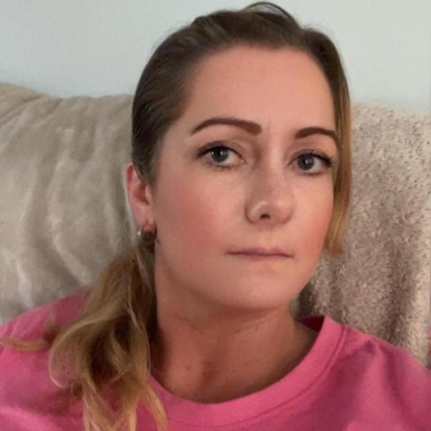 Angela Shellis, a woman with light brown hair pulled back, wearing a pink shirt, looks directly at the camera.
