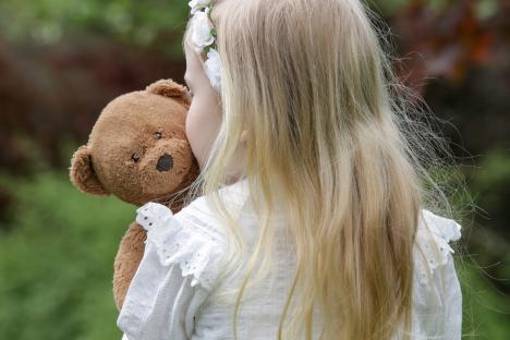 Toddler girl hugging teddy bear in a park.