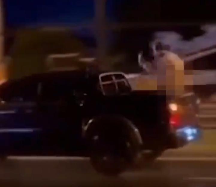 Person riding in the bed of a moving pickup truck at night, with the person censored.