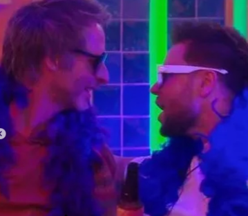 Two men in sunglasses and boas facing each other.