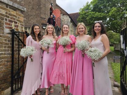 Five bridesmaids in pink and mauve dresses holding bouquets of baby's breath outside a church.