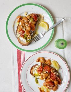 Two slices of toast topped with beans, tomatoes, pesto, and ricotta cheese.