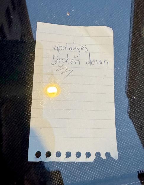 A handwritten note reading "apologies broken down" taped to a car.