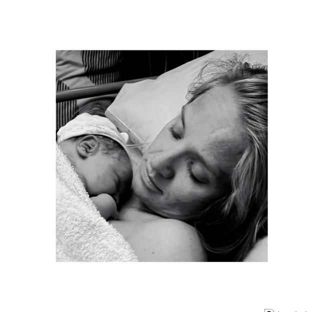A new mother lies with her baby in a black and white photo.
