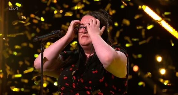 A woman in a cherry-print dress cries while singing on stage, confetti falling around her.