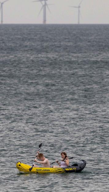Two people kayaking in the ocean with offshore wind turbines in the background.