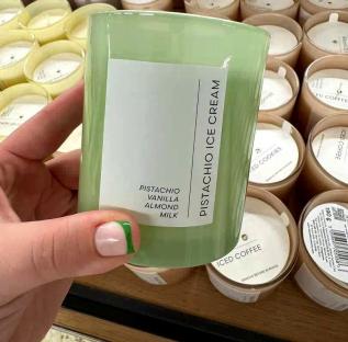 A hand holding a pistachio, vanilla, almond, and milk-scented candle in a Tesco store.