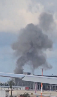 Large plume of smoke rising near an airport building.