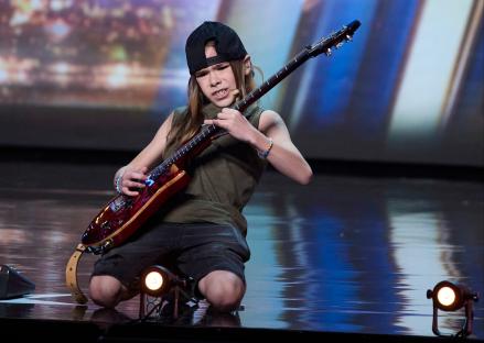 A young person kneeling and playing an electric guitar on a stage.