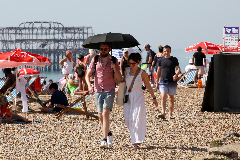Couple sharing an umbrella on a crowded beach.