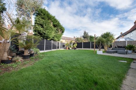 Back garden with lawn, patio furniture, and potted plants.